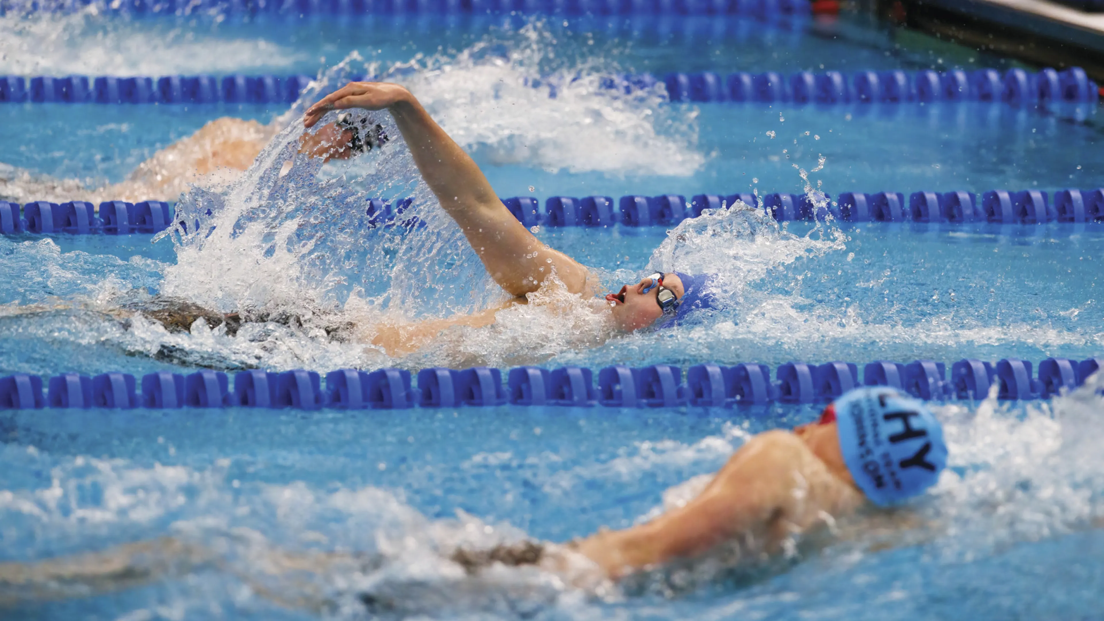 Three male swimmers are seen swimming the backstroke at the Short Course 100th Anniversary YMCA National Championship.