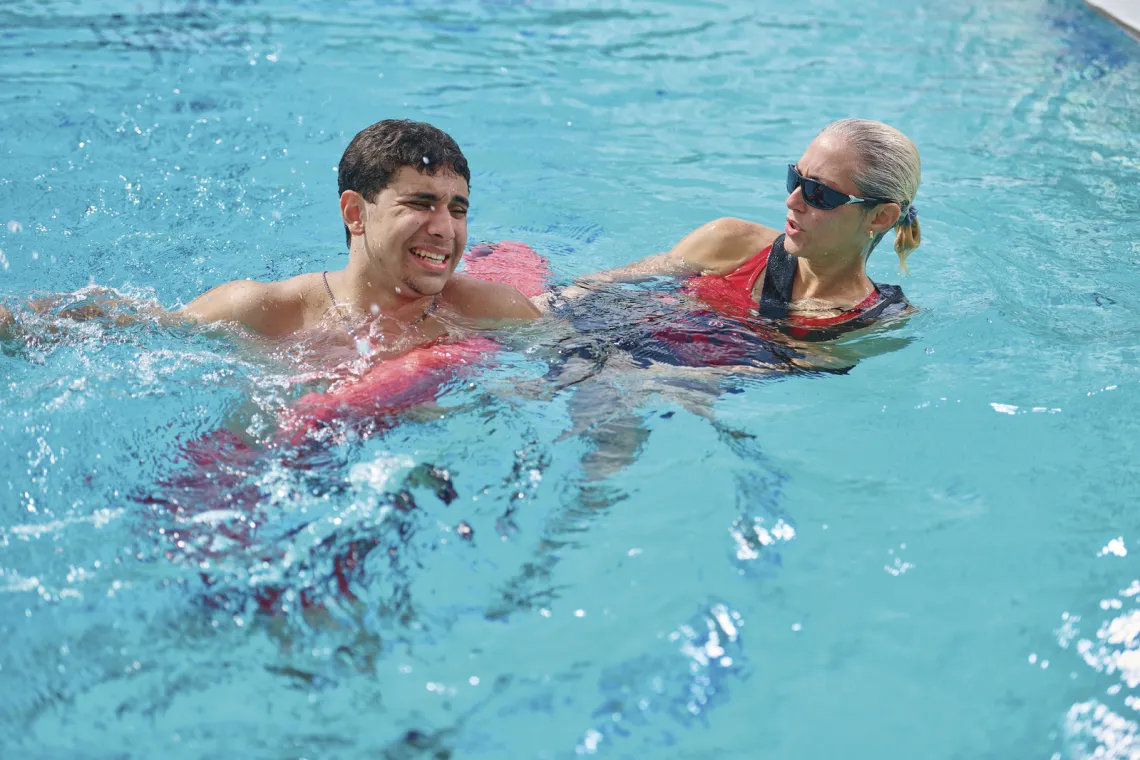 A female lifeguard assists a male swimmer by pulling him to safety with the help of her flotation device.